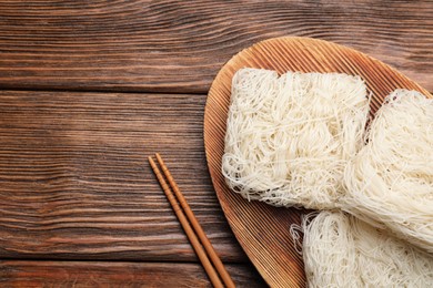 Dried rice noodles with chopsticks on wooden table, flat lay. Space for text
