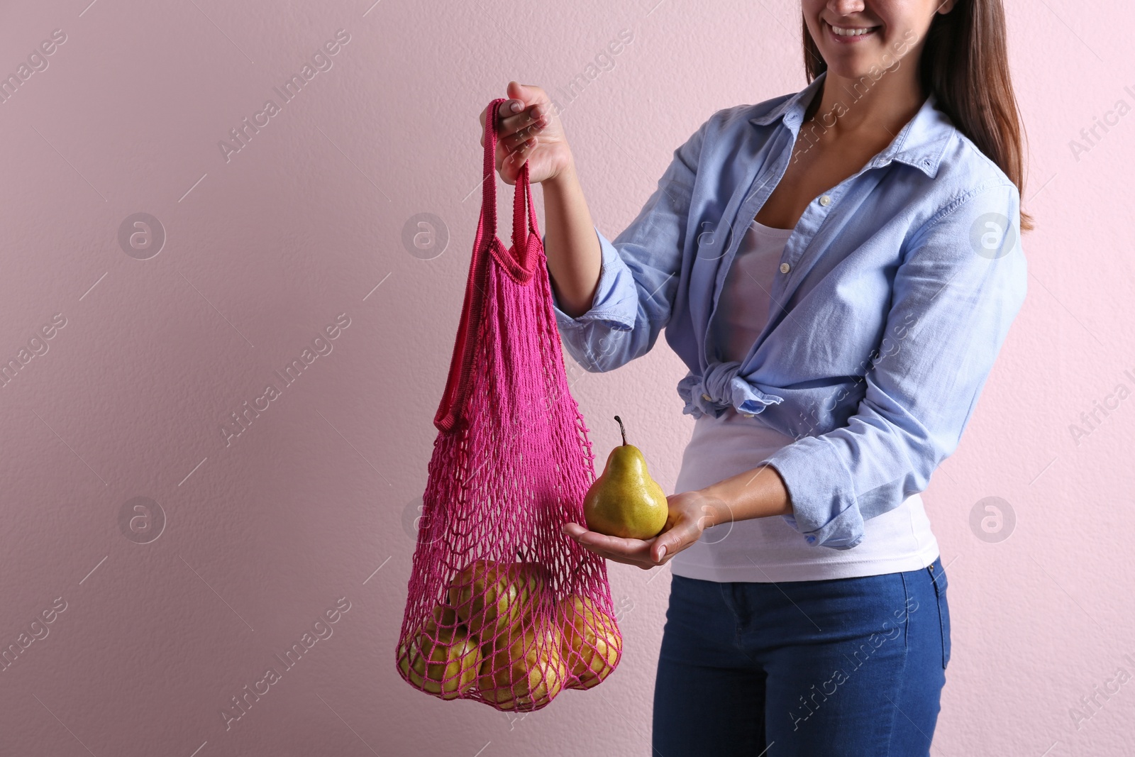 Photo of Woman holding net bag with fresh ripe pears on pink background, closeup