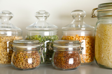 Photo of Different types of legumes and cereals in jars on table. Organic grains
