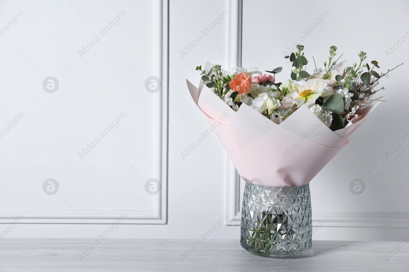 Photo of Bouquet of beautiful flowers in vase on wooden table against white wall. Space for text