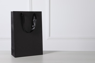 Black paper bag on white wooden table, space for text