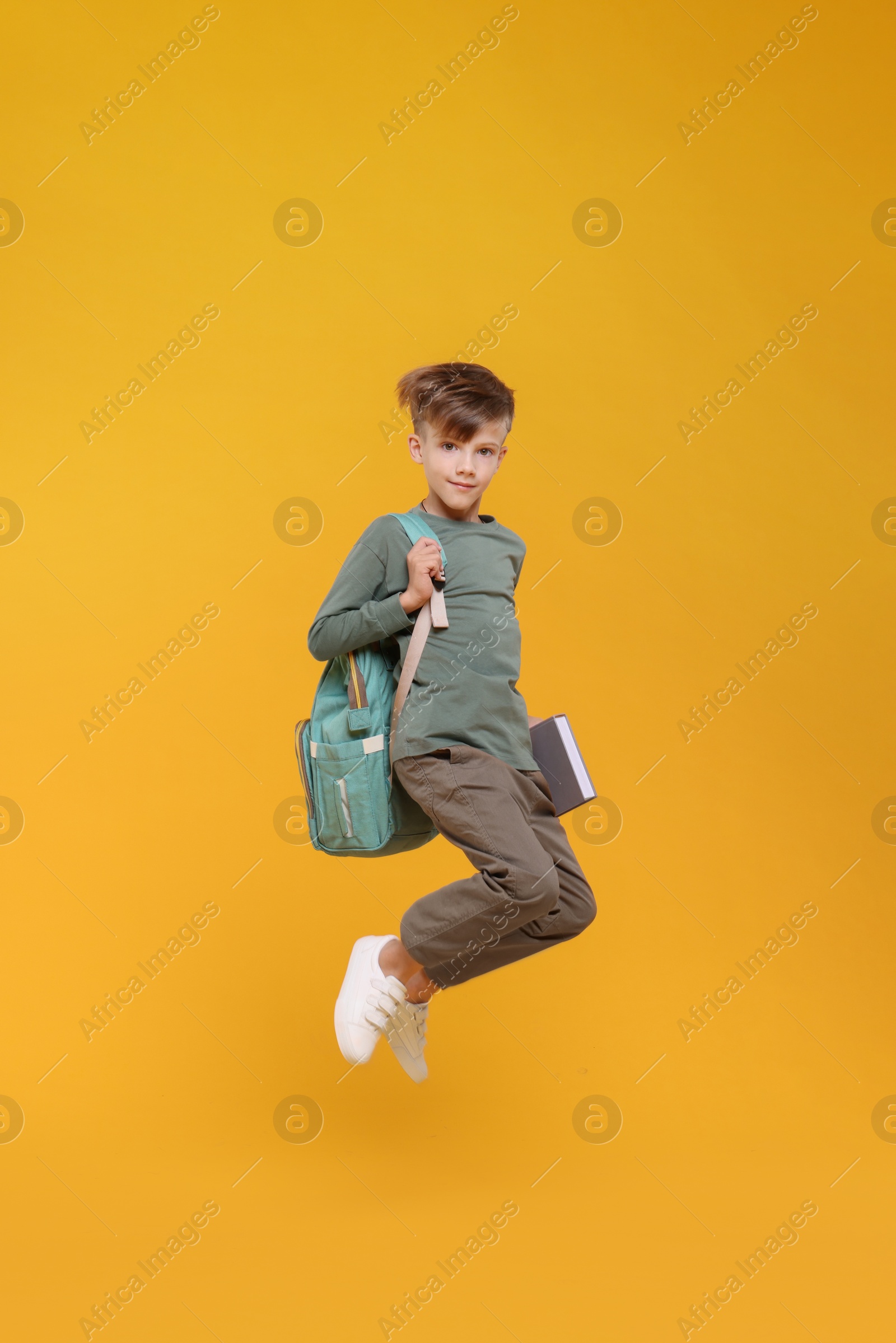 Photo of Cute schoolboy with book jumping on orange background