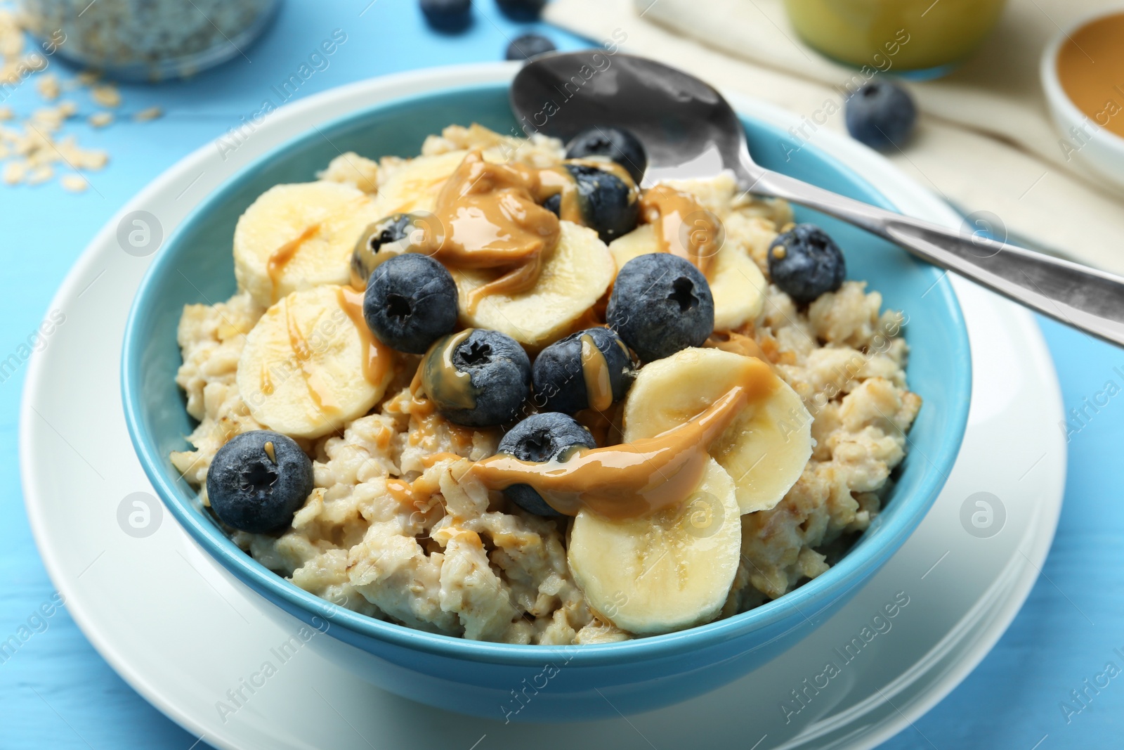 Photo of Tasty oatmeal with banana, blueberries and peanut butter served in bowl on light blue wooden table, closeup