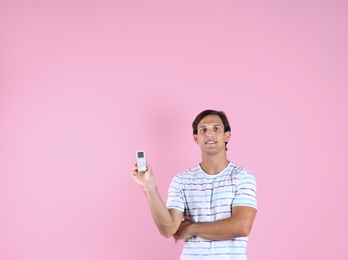 Photo of Young man with air conditioner remote on color background, copy space text