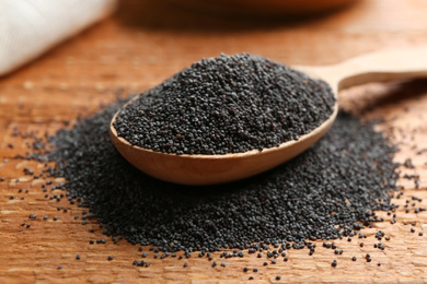 Poppy seeds and spoon on wooden table, closeup