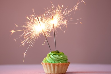 Photo of Cupcake with burning sparklers on pink background