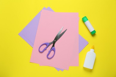 Glue, colorful paper and scissors on yellow background, flat lay