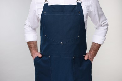 Man wearing kitchen apron on grey background, closeup. Mockup for design