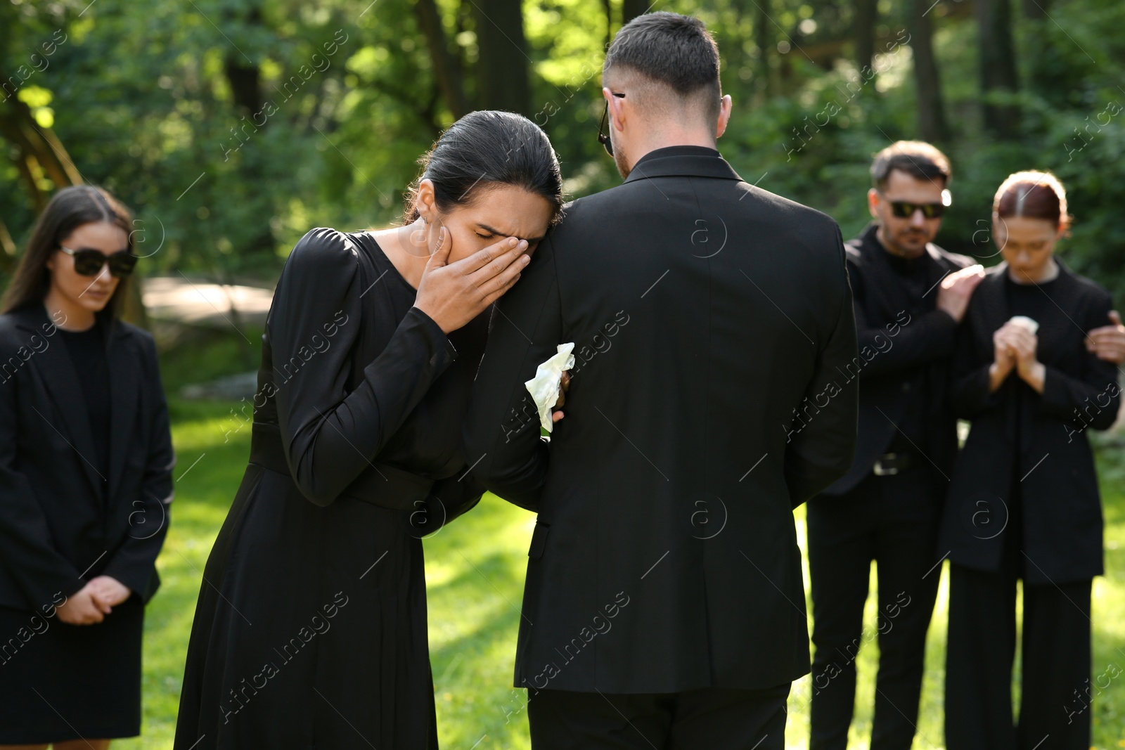 Photo of Sad people in black clothes mourning outdoors. Funeral ceremony