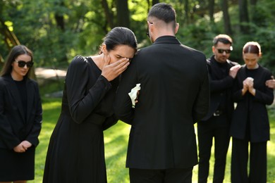 Photo of Sad people in black clothes mourning outdoors. Funeral ceremony