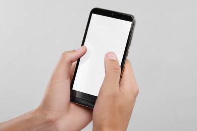 Man typing message on smartphone with blank screen against light grey background, closeup. Mockup for design