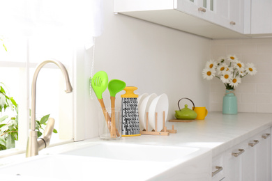 Photo of Kitchenware and flowers on counter indoors. Interior design