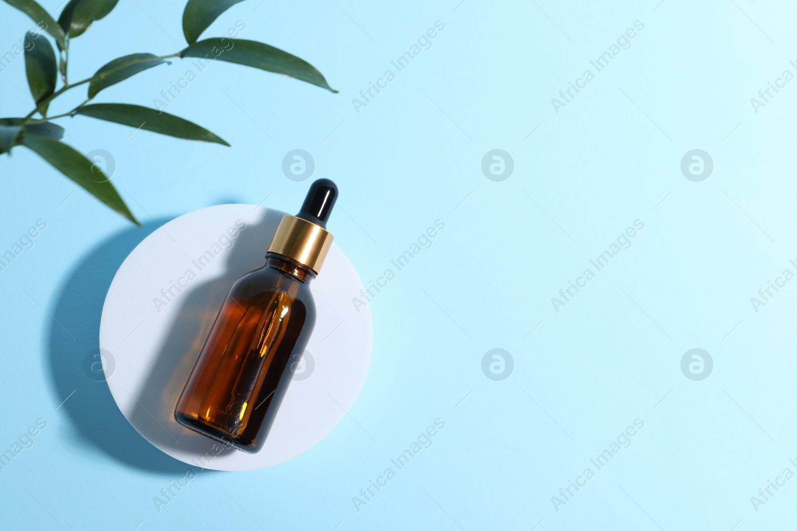 Photo of Bottle with cosmetic oil on podium and green leaves on light blue background, flat lay. Space for text
