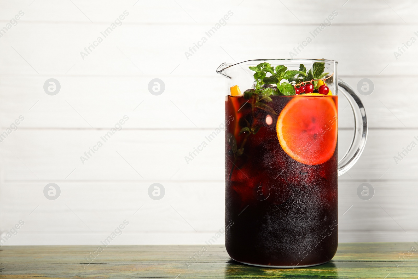 Photo of Jug with delicious refreshing cocktail on table against wooden background