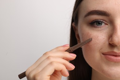 Photo of Beautiful woman drawing freckles with pen on light background, closeup
