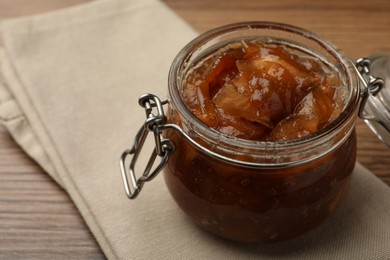 Tasty apple jam in glass jar on wooden table, closeup