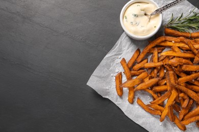 Photo of Delicious sweet potato fries and sauce on black table, top view. Space for text