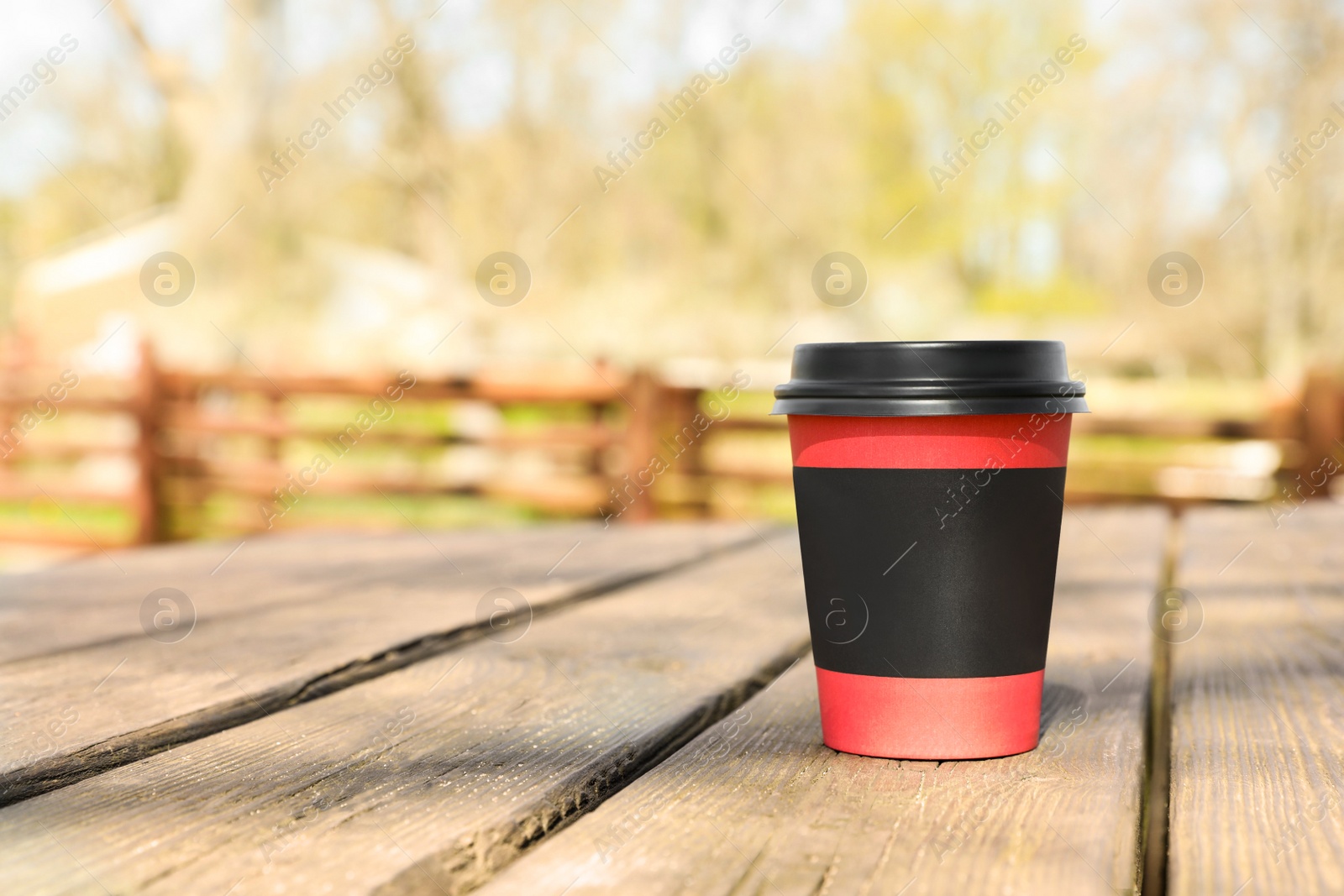 Photo of Hot coffee in takeaway paper cup on wooden table outdoors, space for text