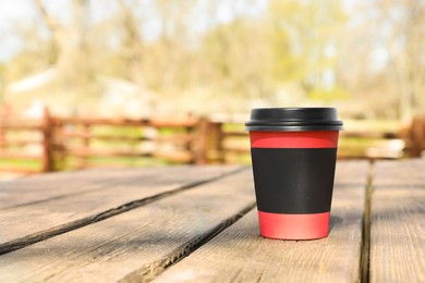 Photo of Hot coffee in takeaway paper cup on wooden table outdoors, space for text