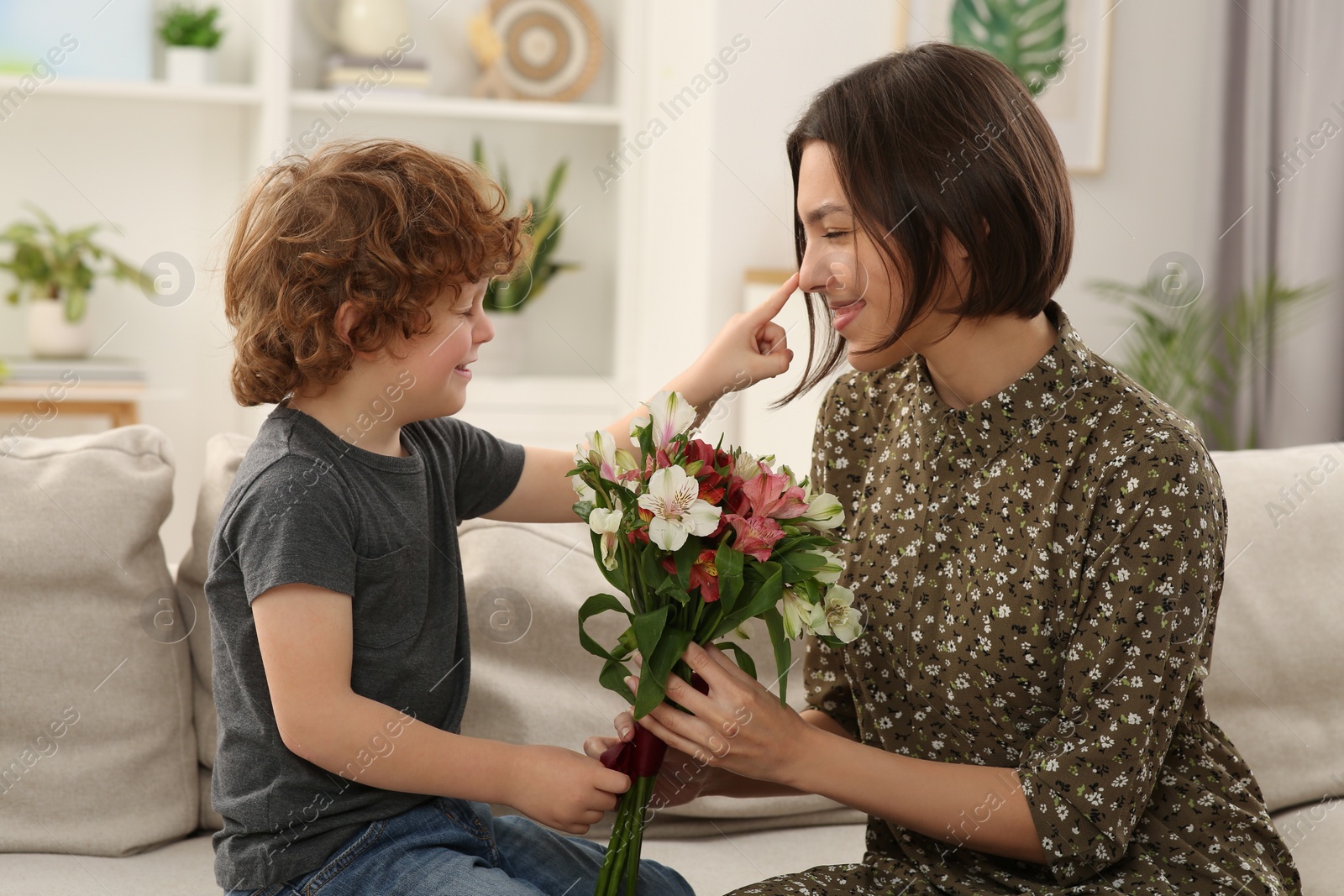 Photo of Little son congratulating his mom with Mother`s day at home. Woman holding bouquet of flowers