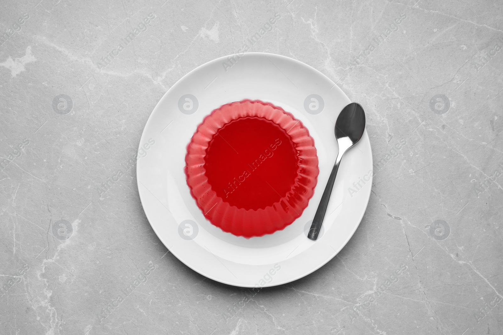 Photo of Plate with tasty fruit jelly and spoon on grey table, top view