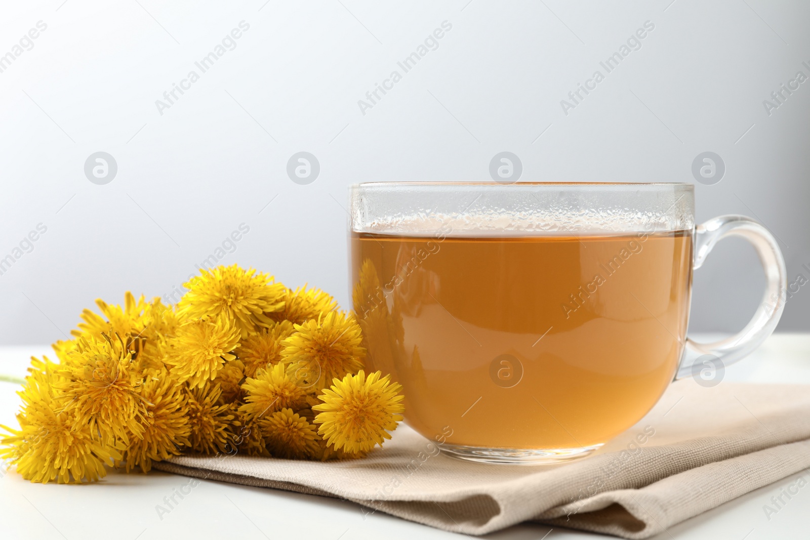 Photo of Delicious fresh tea and beautiful dandelion flowers on white table