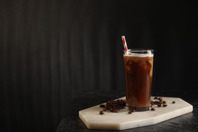 Refreshing iced coffee with milk in glass and beans on table against dark gray background, space for text