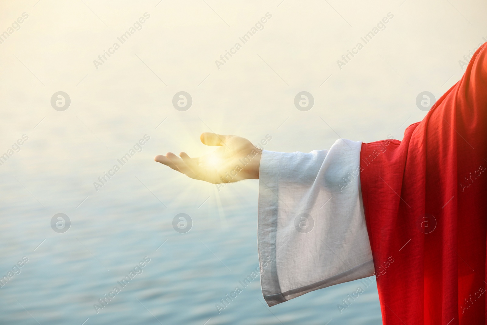 Image of Jesus Christ near water outdoors, closeup. Miraculous light in hand