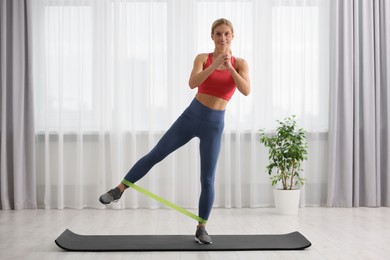 Photo of Athletic woman doing exercise with fitness elastic band on mat at home