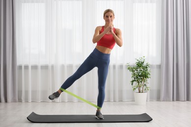 Athletic woman doing exercise with fitness elastic band on mat at home