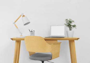 Photo of Stylish office interior with comfortable chair, desk, laptop and lamp