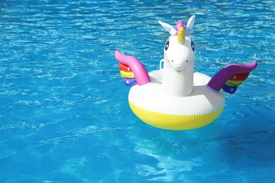 Photo of Funny inflatable unicorn ring floating in swimming pool on sunny day. Space for text