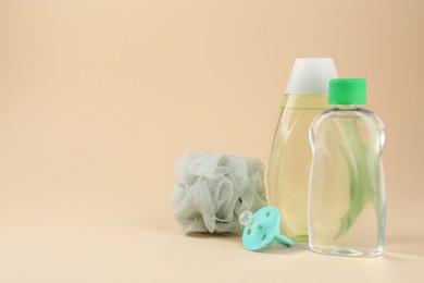 Photo of Bottles with skin care products for baby, shower puff and pacifier on beige background. Space for text