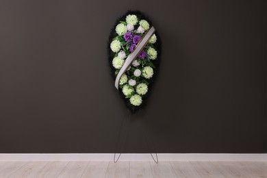 Funeral wreath of plastic flowers with ribbon hanging on dark grey wall indoors
