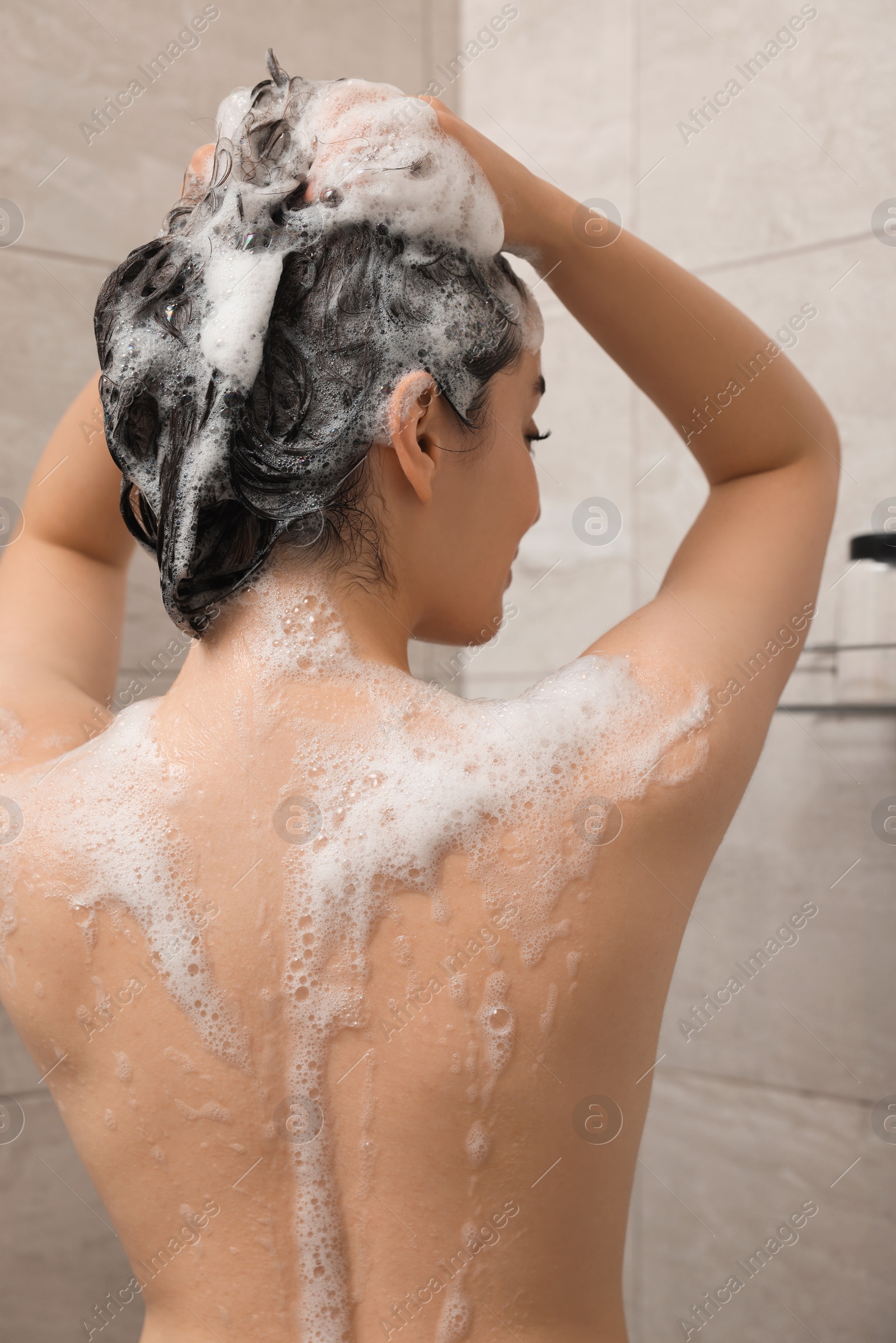 Photo of Woman washing hair in shower, back view