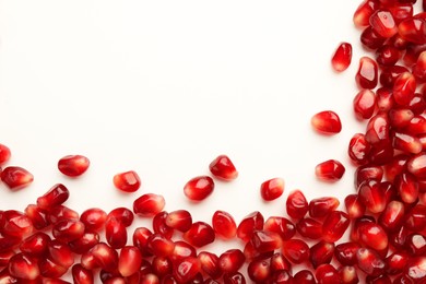 Many ripe juicy pomegranate grains on white background, flat lay. Space for text