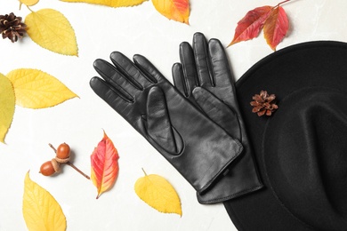 Stylish black leather gloves, hat and dry leaves on white table, flat lay