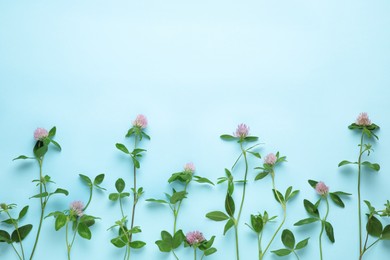 Beautiful clover flowers with green leaves on turquoise background, flat lay. Space for text