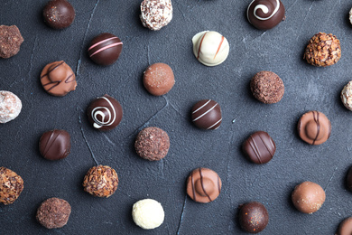 Different tasty chocolate candies on black table, flat lay