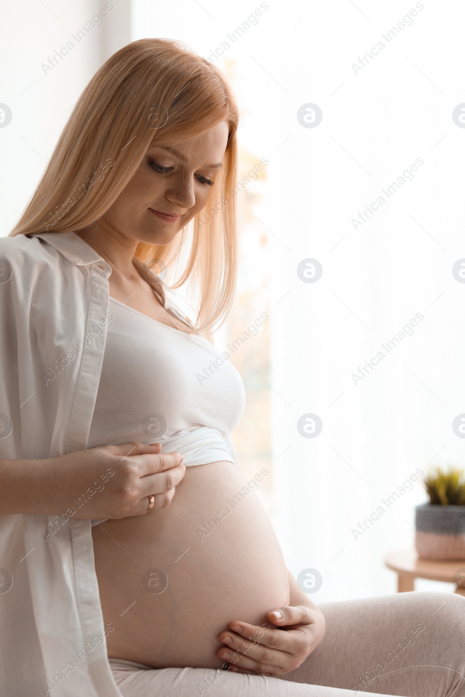 Photo of Beautiful pregnant woman sitting in light room at home