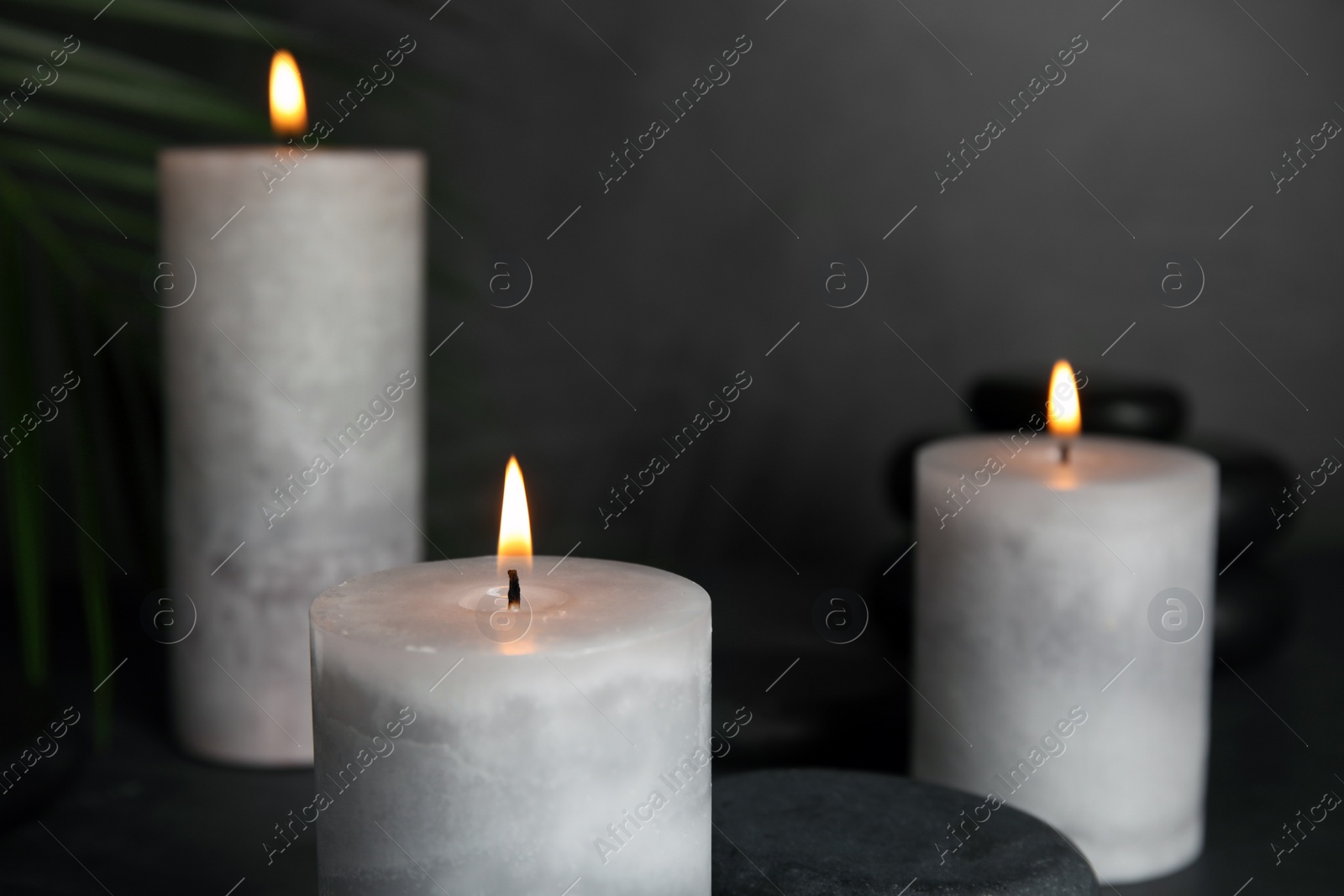 Photo of Burning candles, spa stones and palm leaf on grey background