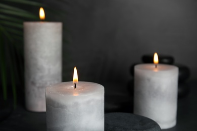 Burning candles, spa stones and palm leaf on grey background