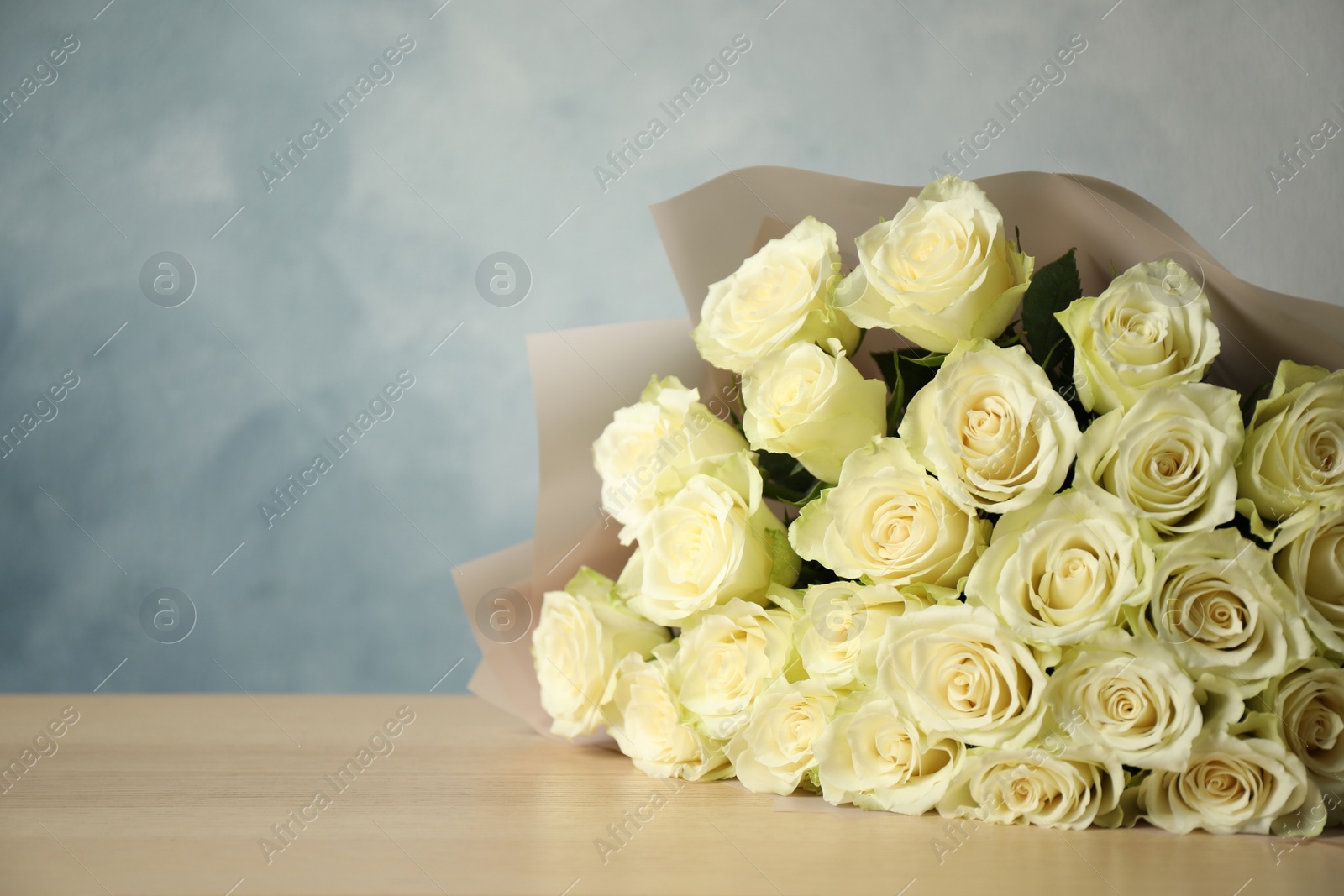 Photo of Luxury bouquet of fresh roses on wooden table, space for text