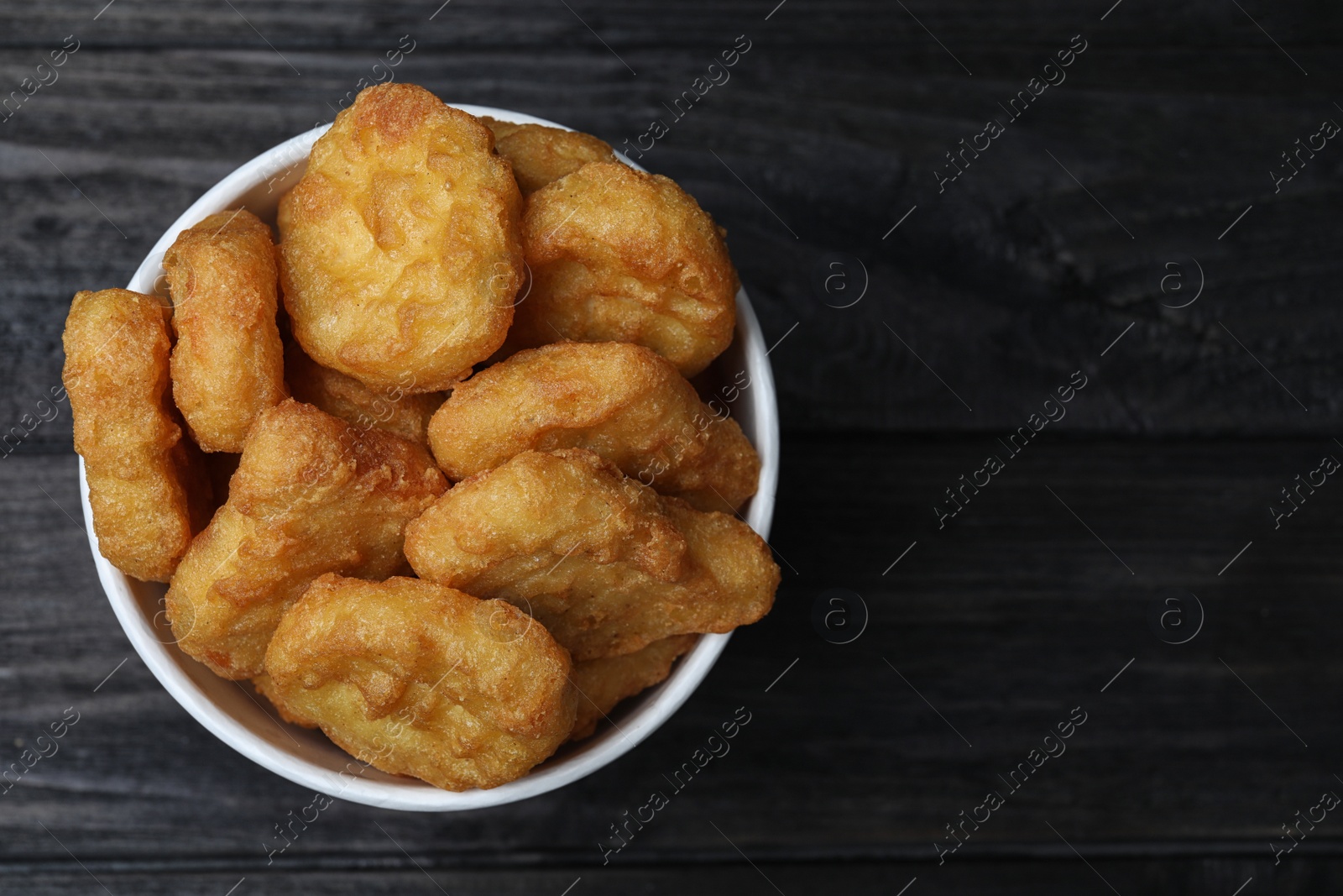 Photo of Bucket with tasty chicken nuggets on black wooden table, top view. Space for text
