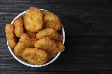 Photo of Bucket with tasty chicken nuggets on black wooden table, top view. Space for text