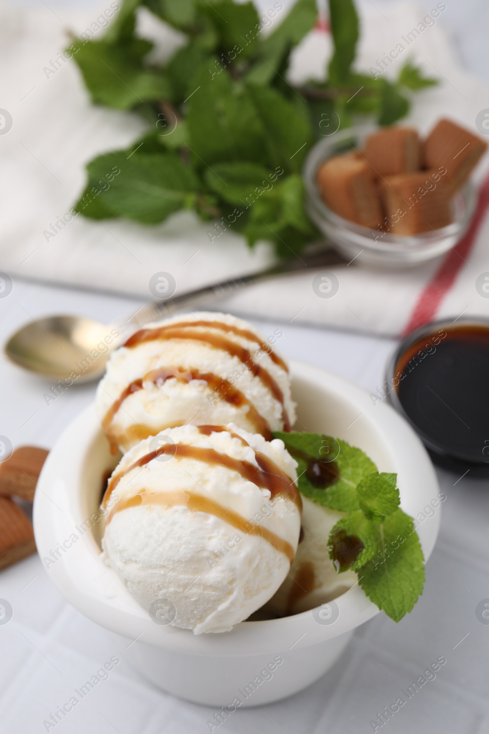 Photo of Scoops of tasty ice cream with mint leaves and caramel sauce on white tiled table