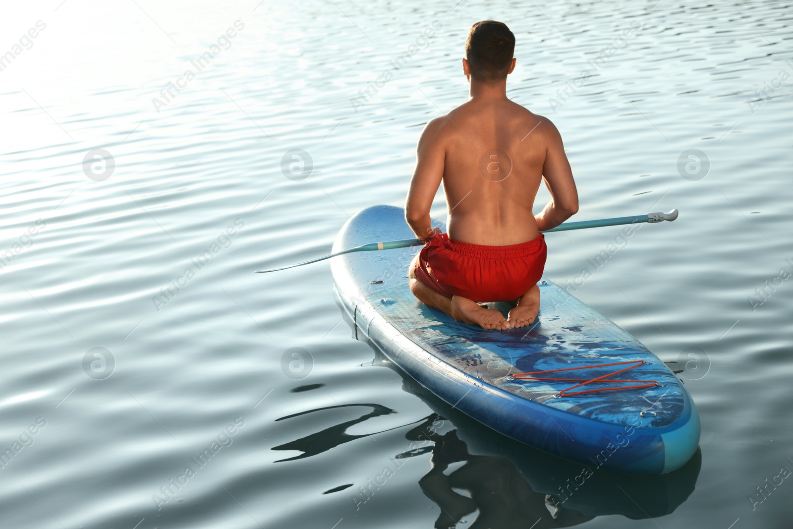 Photo of Man paddle boarding on SUP board in river at sunset, back view