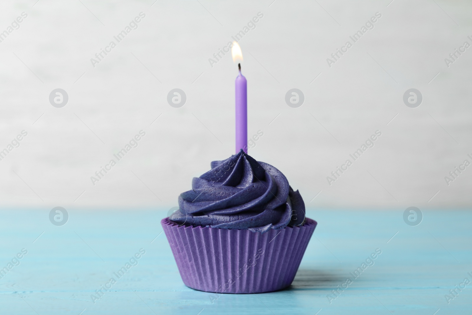 Photo of Delicious birthday cupcake with cream and burning candle on blue wooden table