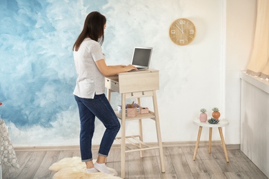 Photo of Young woman using laptop at stand up workplace in room