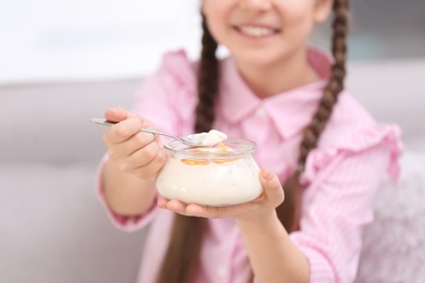 Cute girl eating tasty yogurt at home